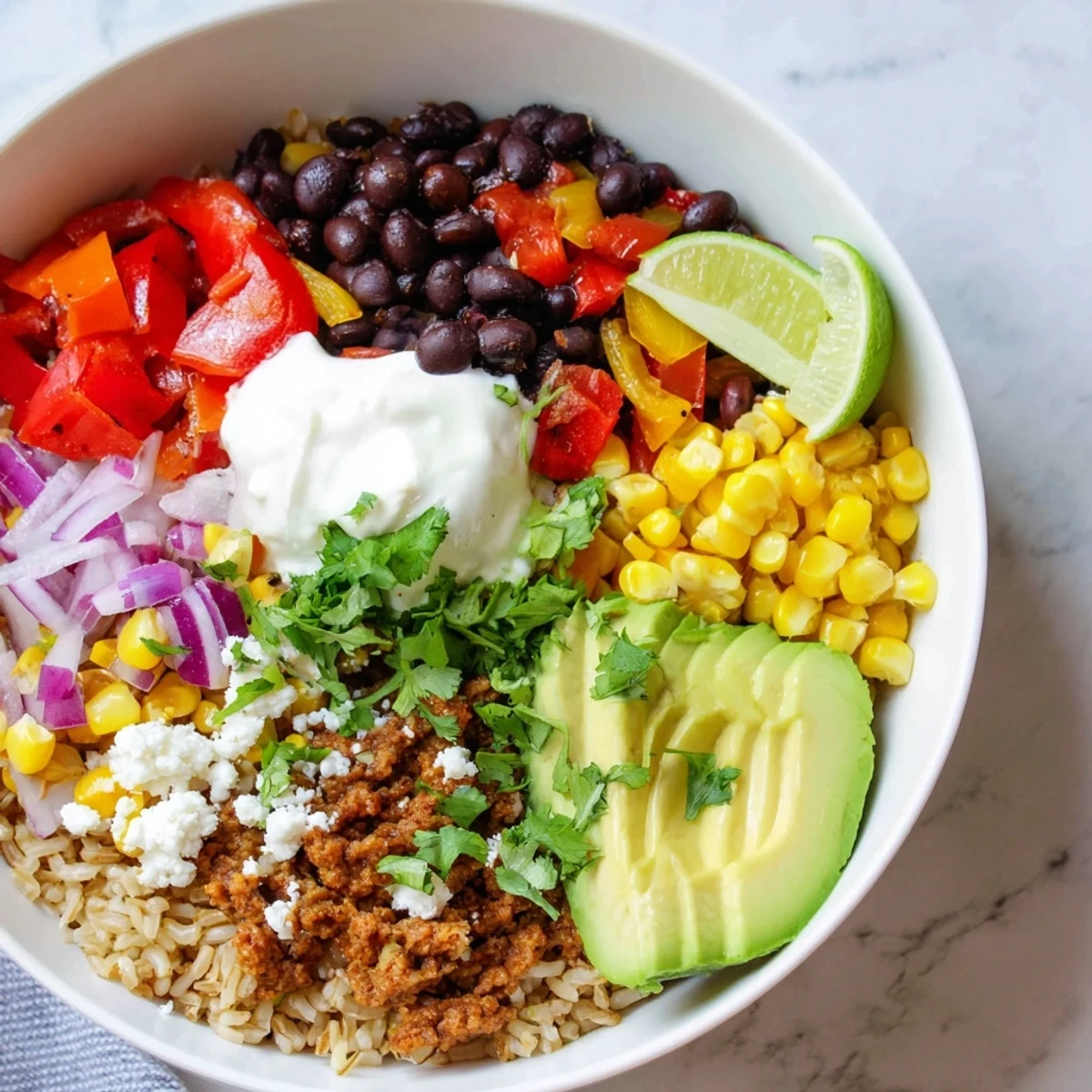 Hearty brown rice burrito bowl loaded with seasoned beans, crisp onions, and a dollop of tangy sour cream, ready to enjoy.