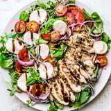 A fresh, colorful Caprese Chicken Salad features grilled chicken with ripe tomatoes, creamy mozzarella, and basil.
