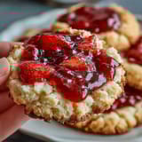 Fresh strawberry jam thumbprint cookies with golden edges and ruby-red centers, ready for a sweet treat.