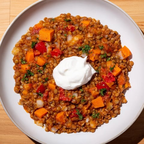 Steaming, hearty Wheat-Warm Hearty Lentil Curry sits in a bowl, garnished with fresh cilantro and yogurt.