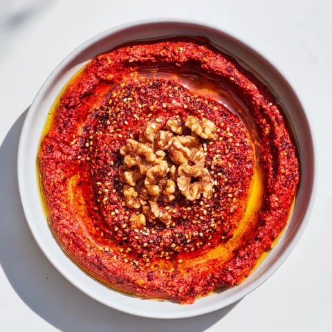 Smoky Syrian Muhammara dip, a vibrant red color, served with warm pita bread for dipping.