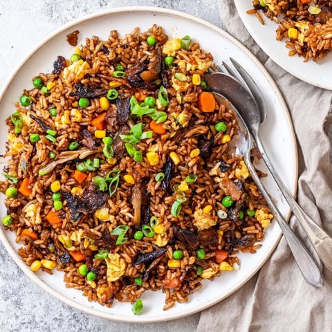 Sizzling black garlic fried rice in a hot wok, with steam rising and colorful mixed vegetables like peas and carrots.