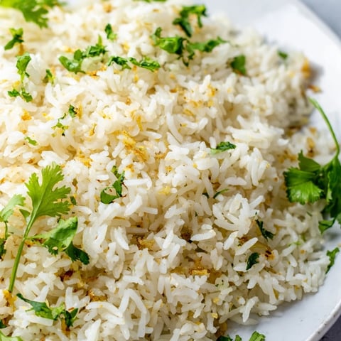 Fluffy, steaming Jasmine Rice Garlic with golden toasted garlic pieces and fresh cilantro garnish.