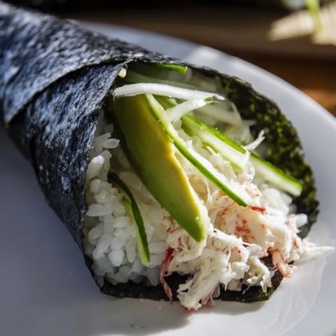 A close-up photo of a Sushi Rice Hand Roll filled with creamy avocado, crisp cucumber, and sweet crab, ready to be served.