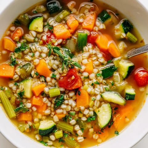 Steaming bowl of simple homemade grain and vegetable soup, filled with colorful, tender vegetables.