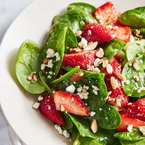 A close-up of a refreshing strawberry spinach salad, showing off textures and toasted almonds.