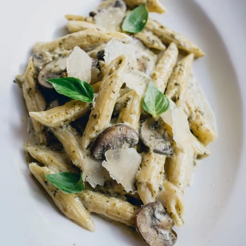 Sautéed cremini mushrooms and penne tossed in a vibrant basil pesto cream sauce for dinner.