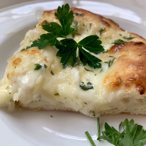 A close-up of Creamy Garlic White Pizza with golden, bubbly cheese and a garlic cream sauce on a rustic wooden board.