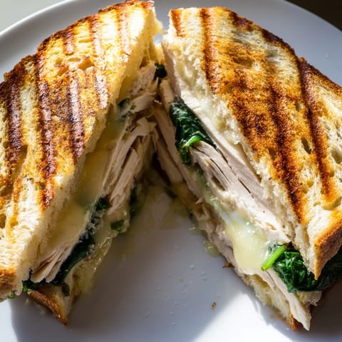 Close-up of a Grilled Chicken Spinach Panini, oozing melted cheese and spinach, with garlic butter on crusty bread.  