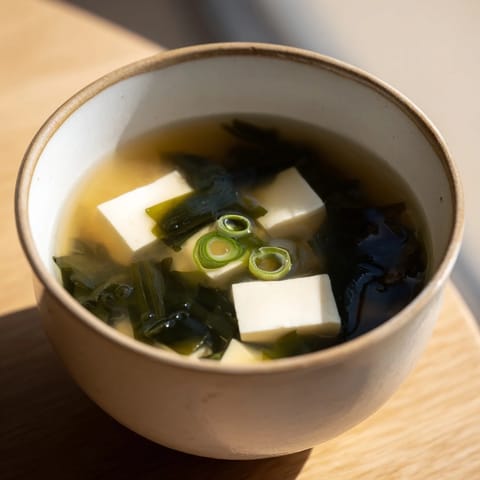Steaming bowl of Miso Soup With Tofu next to chopsticks on a wooden table.