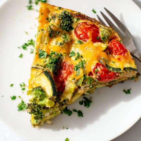 A golden-baked vegetable frittata with broccoli, bell peppers, and melted cheddar cheese, sliced on a rustic platter.