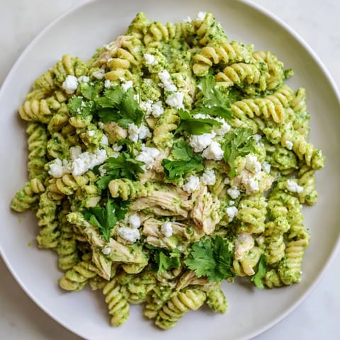 Vibrant Cilantro Lime Chicken Pasta garnished with crumbled feta, fresh cilantro, and lime wedges on a rustic table.