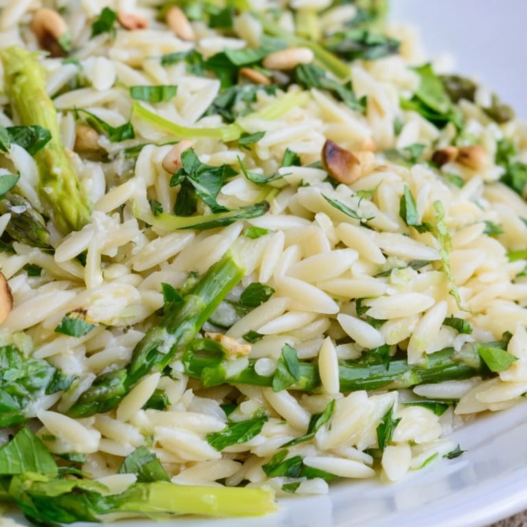 A vibrant bowl of Asparagus Lemon Orzo Salad features bright green asparagus, fluffy orzo, and a sprinkle of Parmesan, ready for a sunny picnic.  